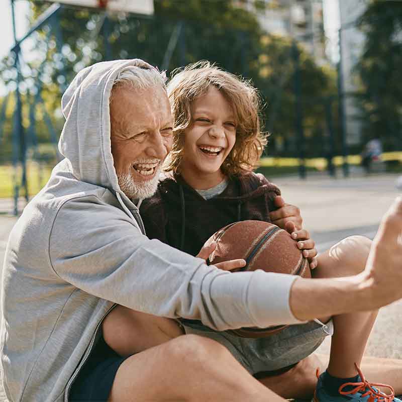Grandfather and grandson laughing on the basketball court. 